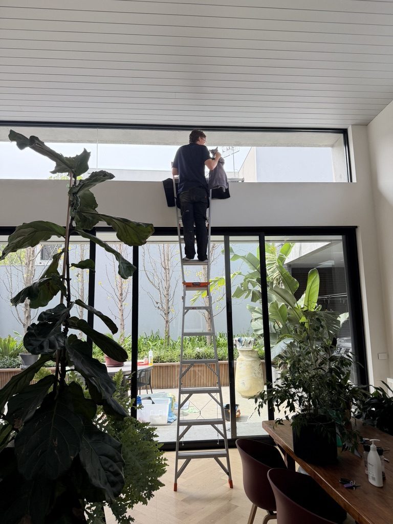 Cleaning a high interior window from a ladder